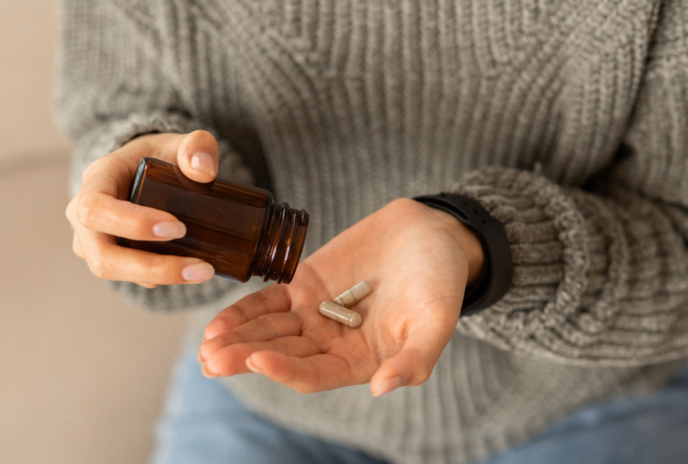 Hands holding pill bottle, two capsules dispensed