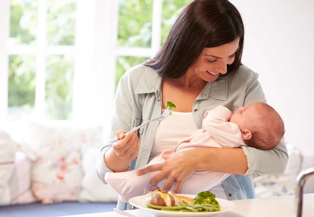 Mother holding baby while eating healthy meal