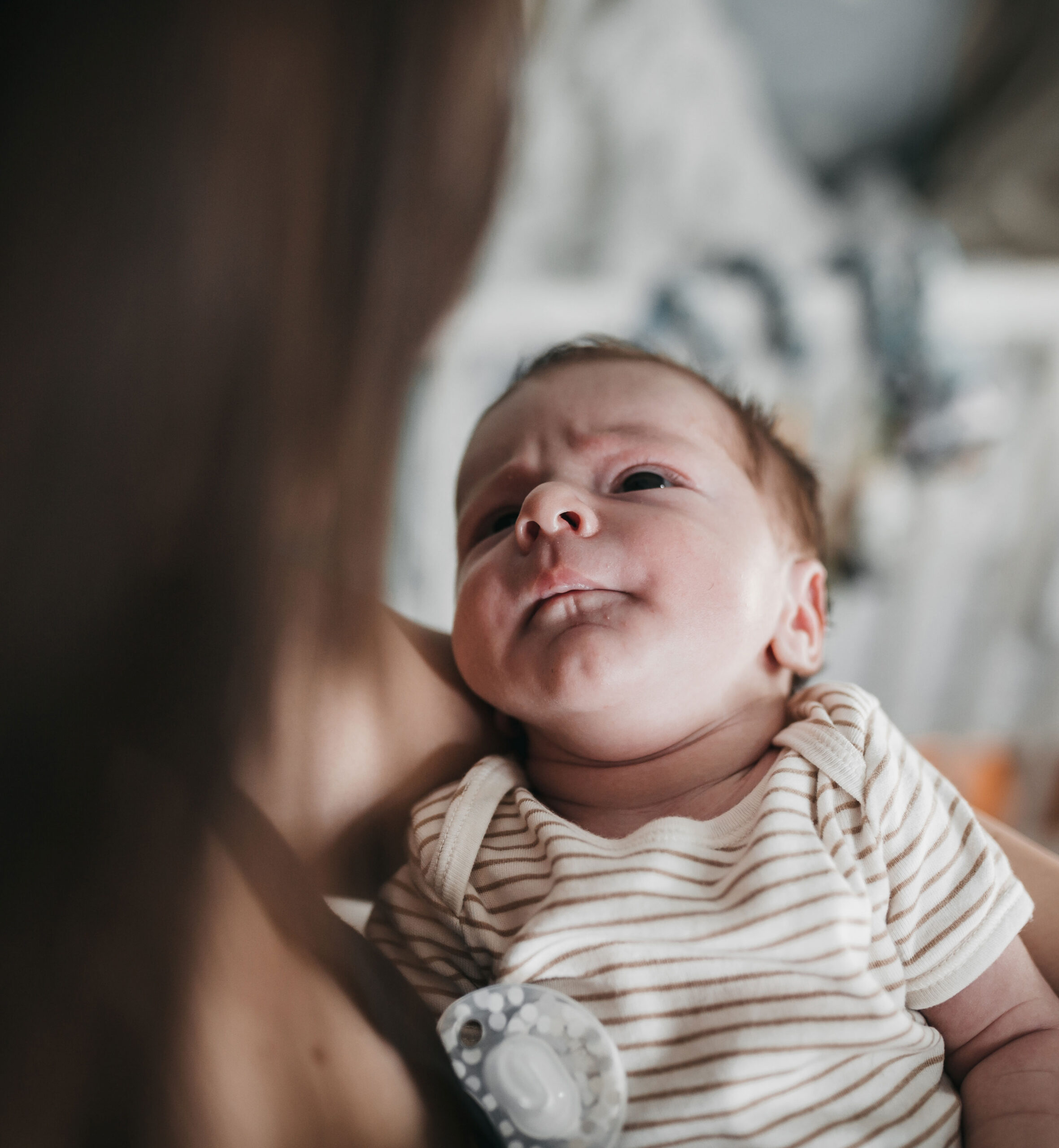 Baby in striped outfit gazing upwards, being held