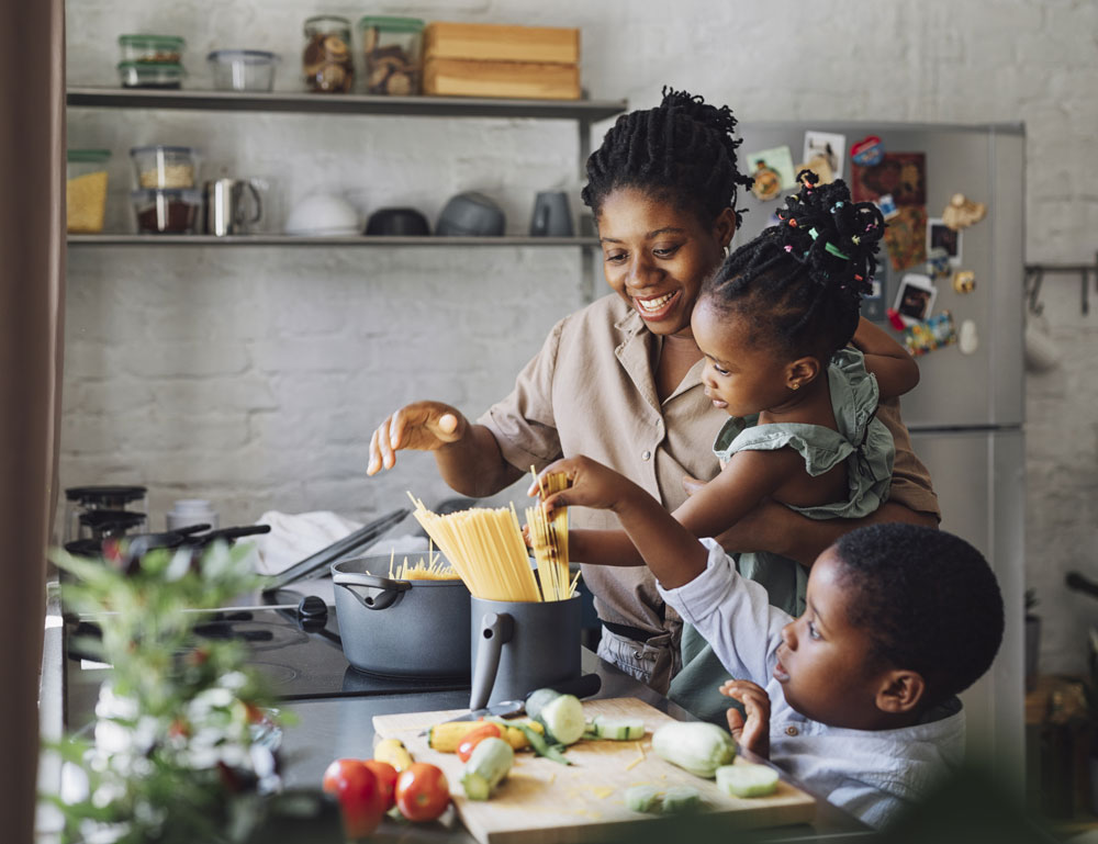 Mother cooking pasta with two young children
