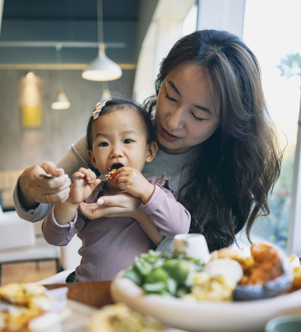 Mother feeding her toddler at a table full of food