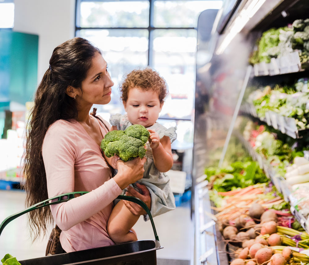 Mother holding baby while grocery shopping with vegetables