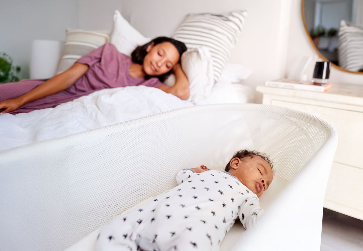 Mother resting on bed, baby sleeping in bassinet